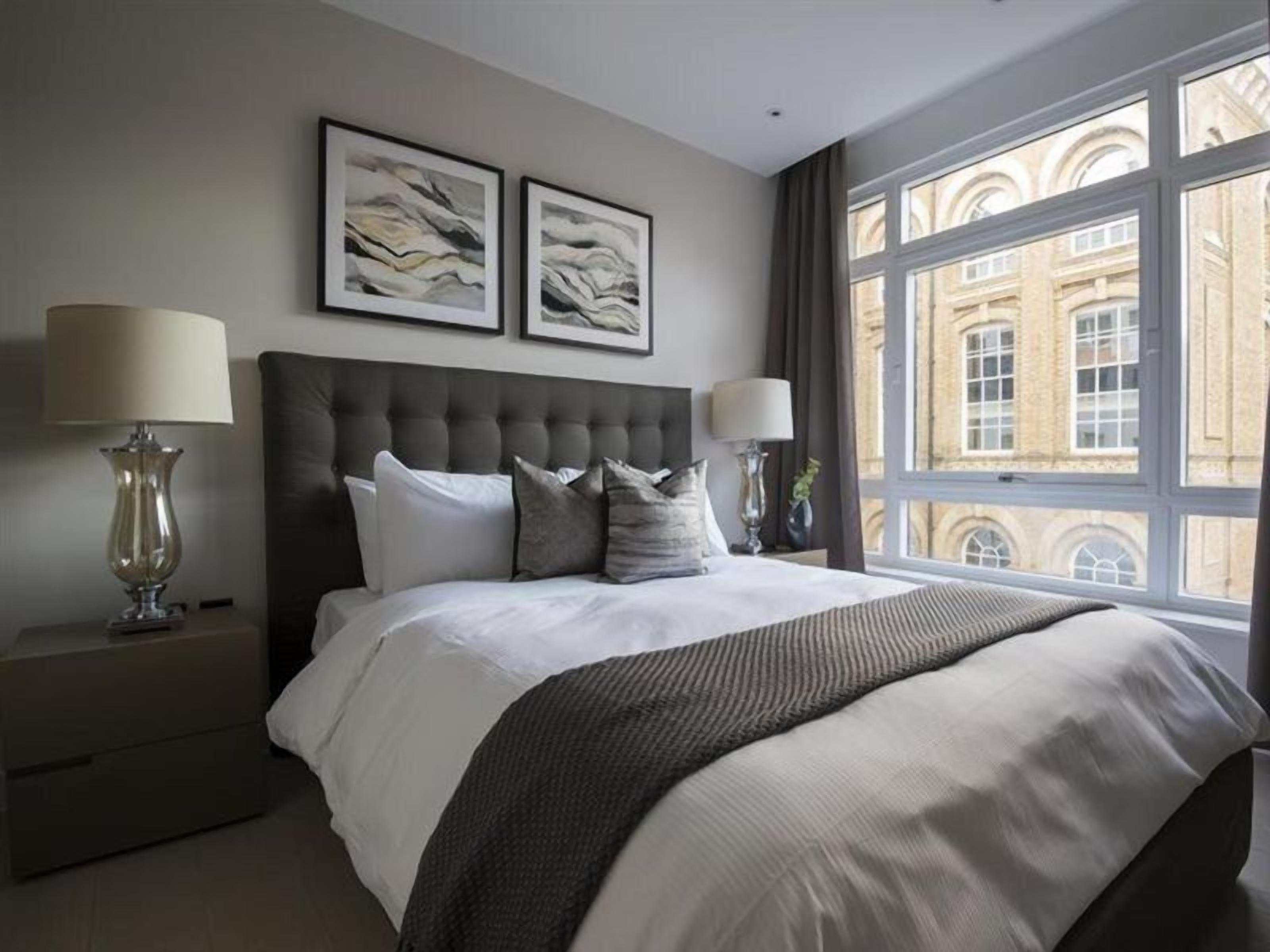 Ein Schlafzimmer mit einem großen Bett, zwei Nachttischlampen und einem Fenster mit Blick auf ein Gebäude.