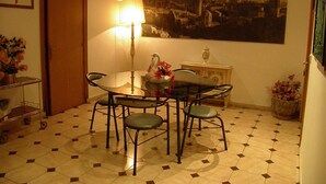 Ein Essbereich mit einem runden Tisch, Stühlen, einer Lampe, einem Stadtbild als Gemälde und einem Fliesenboden.