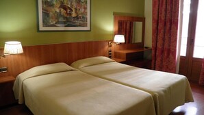 Ein Hotelzimmer mit zwei Betten, einem Bild an der Wand, einem Spiegel und einem Fenster mit Vorhängen.