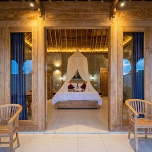 Dormitorio con estructura de madera, cama con dosel, dos sillas y vistas a través de un ventanal.