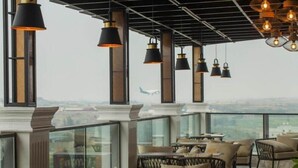 Un espace de détente intérieur avec des tables et des chaises, de grandes fenêtres et des lampes suspendues.