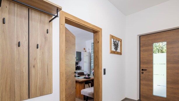 Un corridoio con porte in legno, una sala da pranzo con tavolo e sedie, e vista attraverso una porta in vetro.
