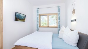 Una camera da letto con un letto di legno, una finestra con tende, un quadro appeso al muro e una lampada da parete.