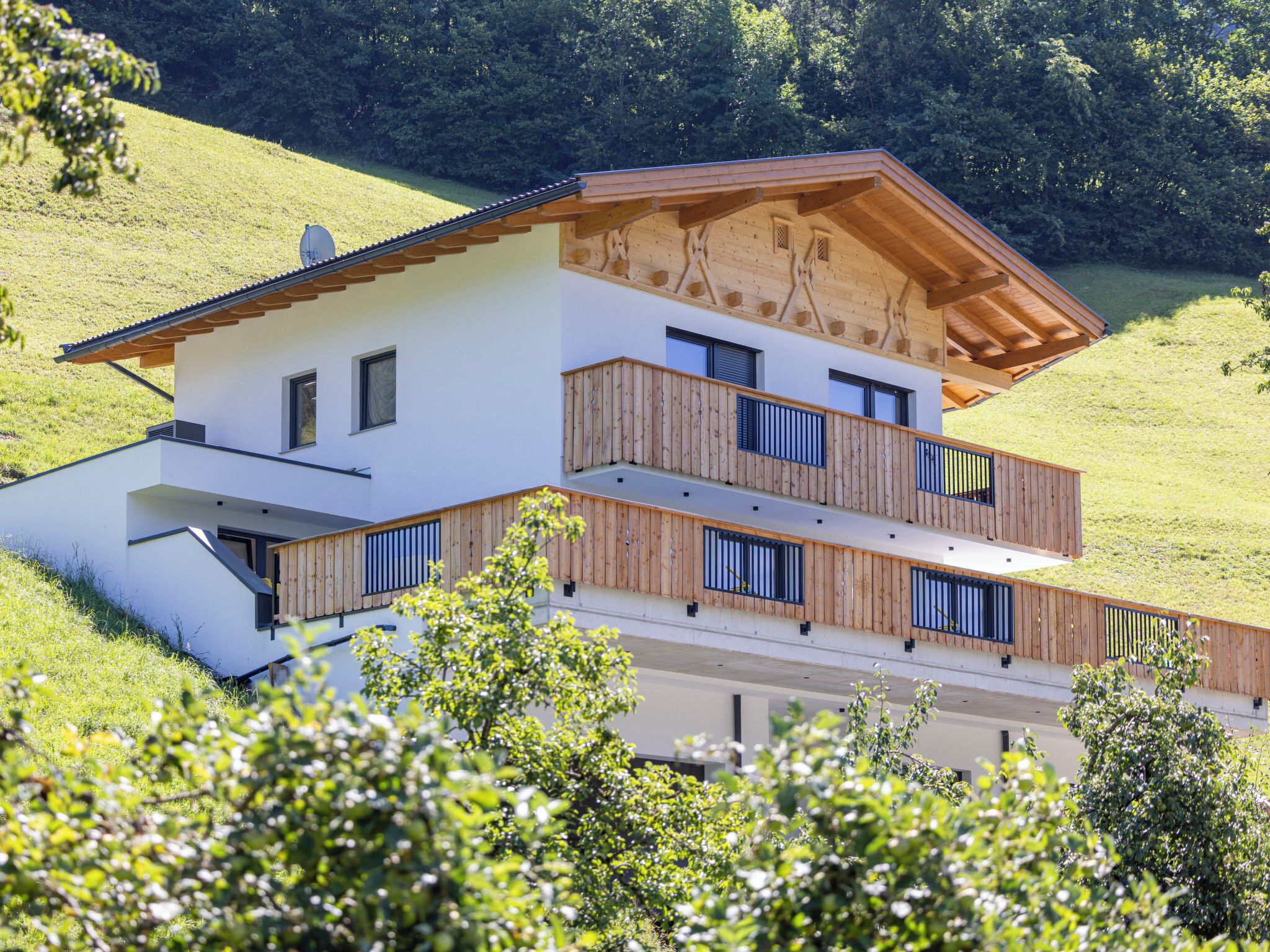 Une maison moderne à deux étages, dotée d’un toit en pente, de balustrades en bois sur le balcon et d’une façade blanche.