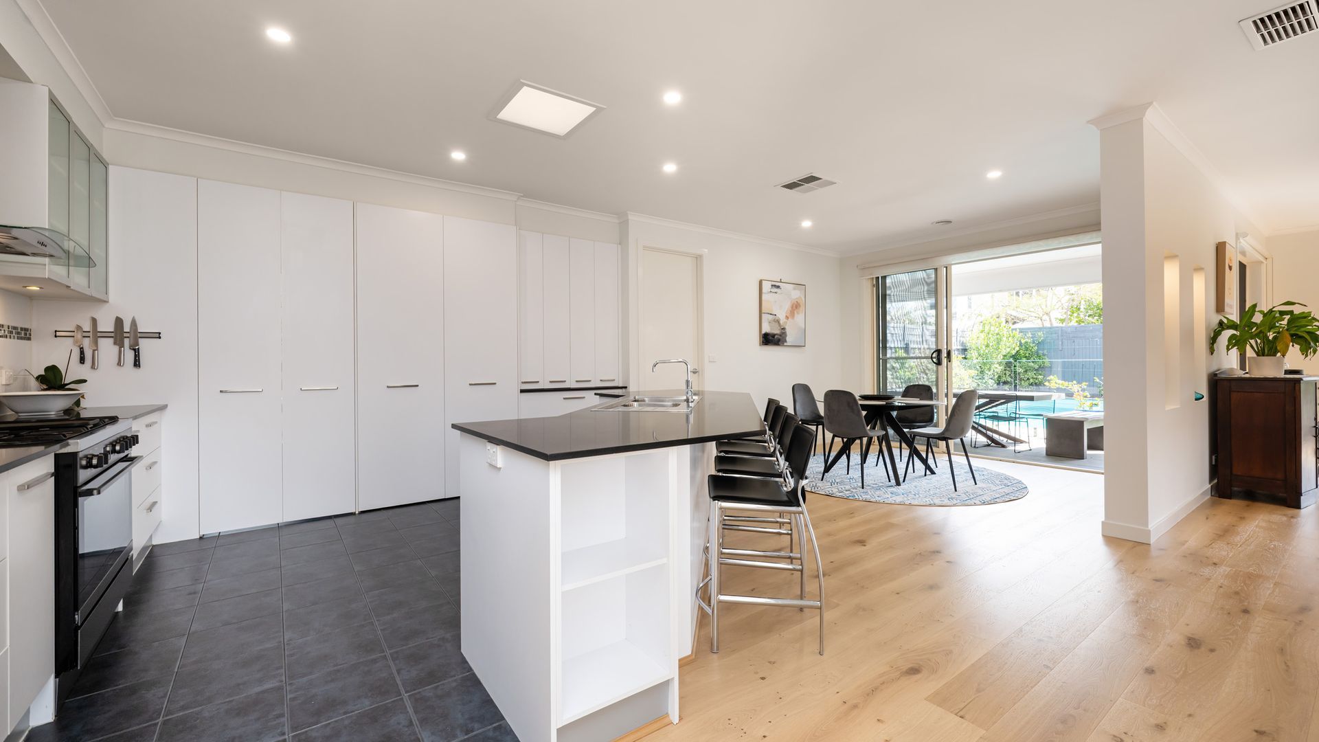 A modern kitchen with white cabinetry, a black countertop island, and a dining area with a round table and chairs.