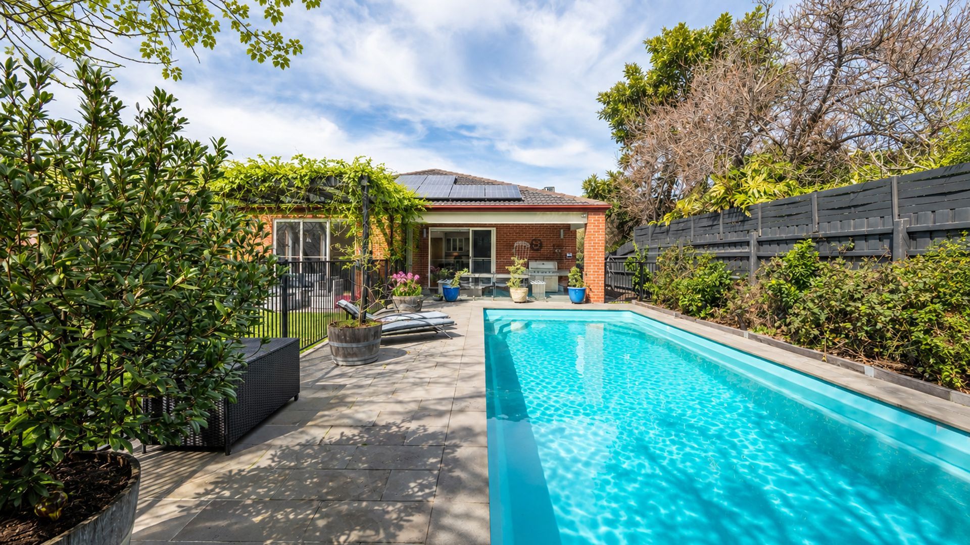 A swimming pool with a patio area, a brick house, and surrounding greenery.