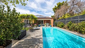 Ein Swimmingpool mit Terrassenbereich, ein Ziegelhaus und umliegendes Grün.