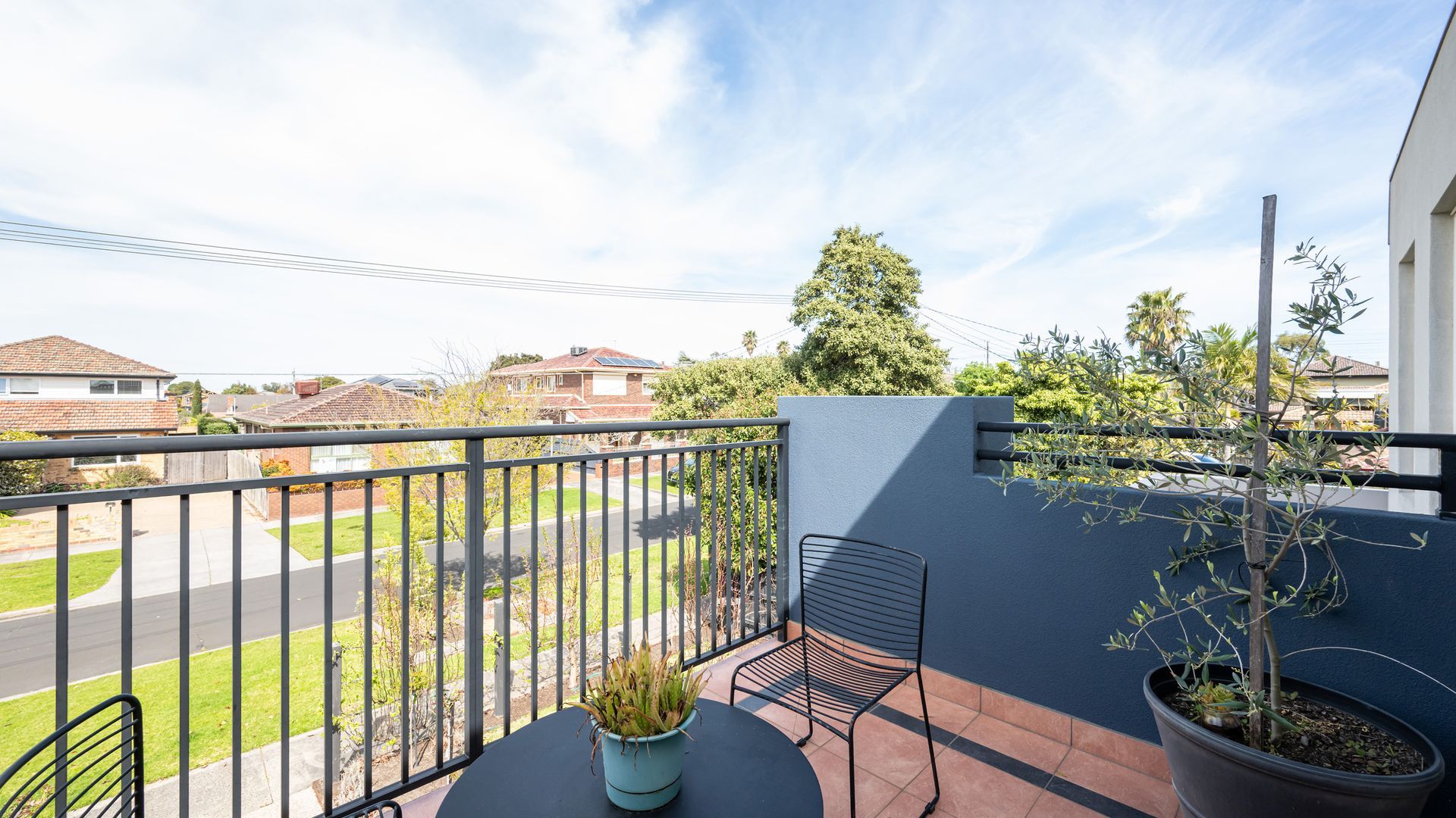 Een balkon met een metalen hekwerk, een bloempot en een stoel.