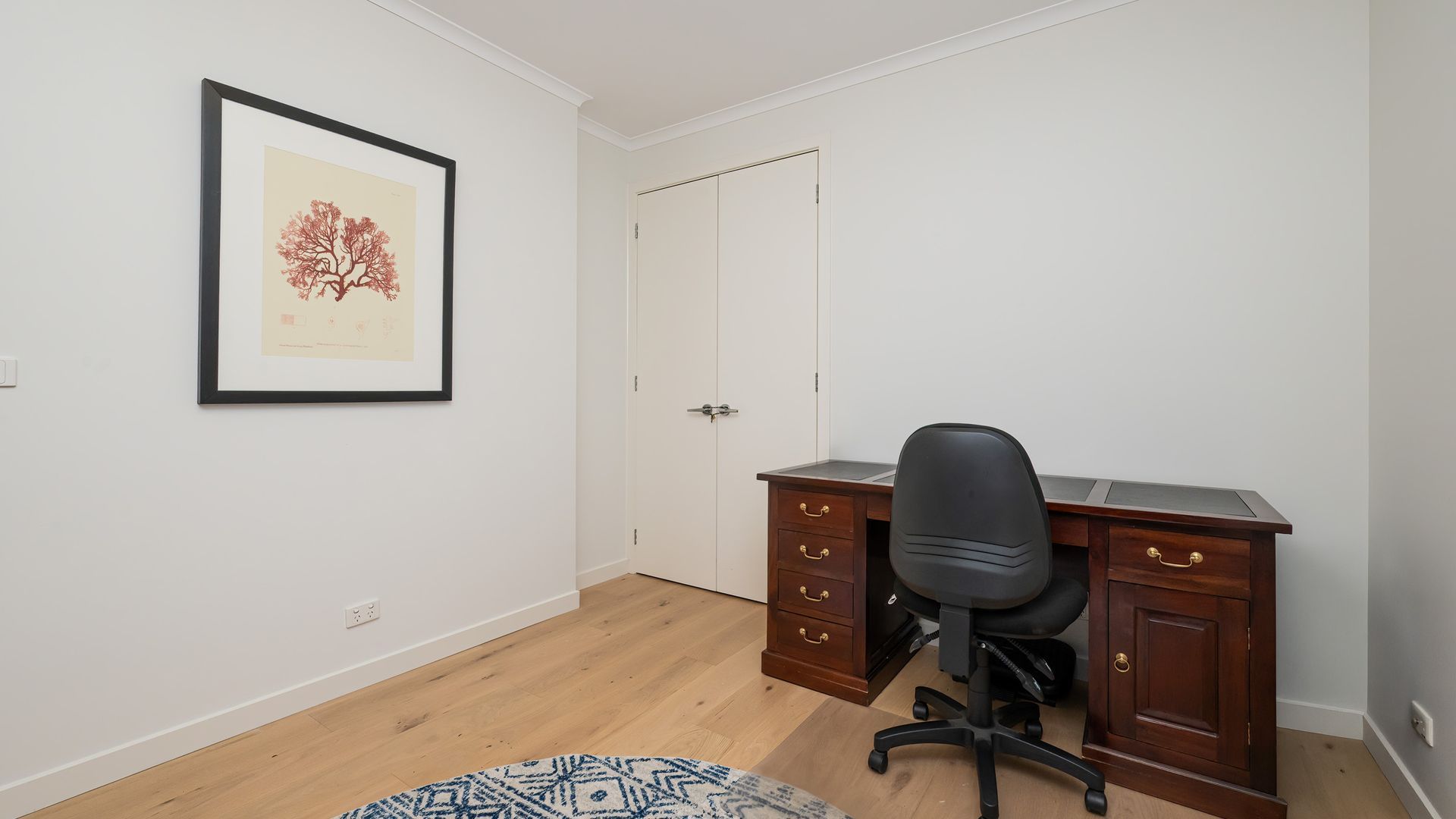 Ein Zimmer mit Schreibtisch, Stuhl, Kleiderschrank und einem gerahmten Bild an der Wand.