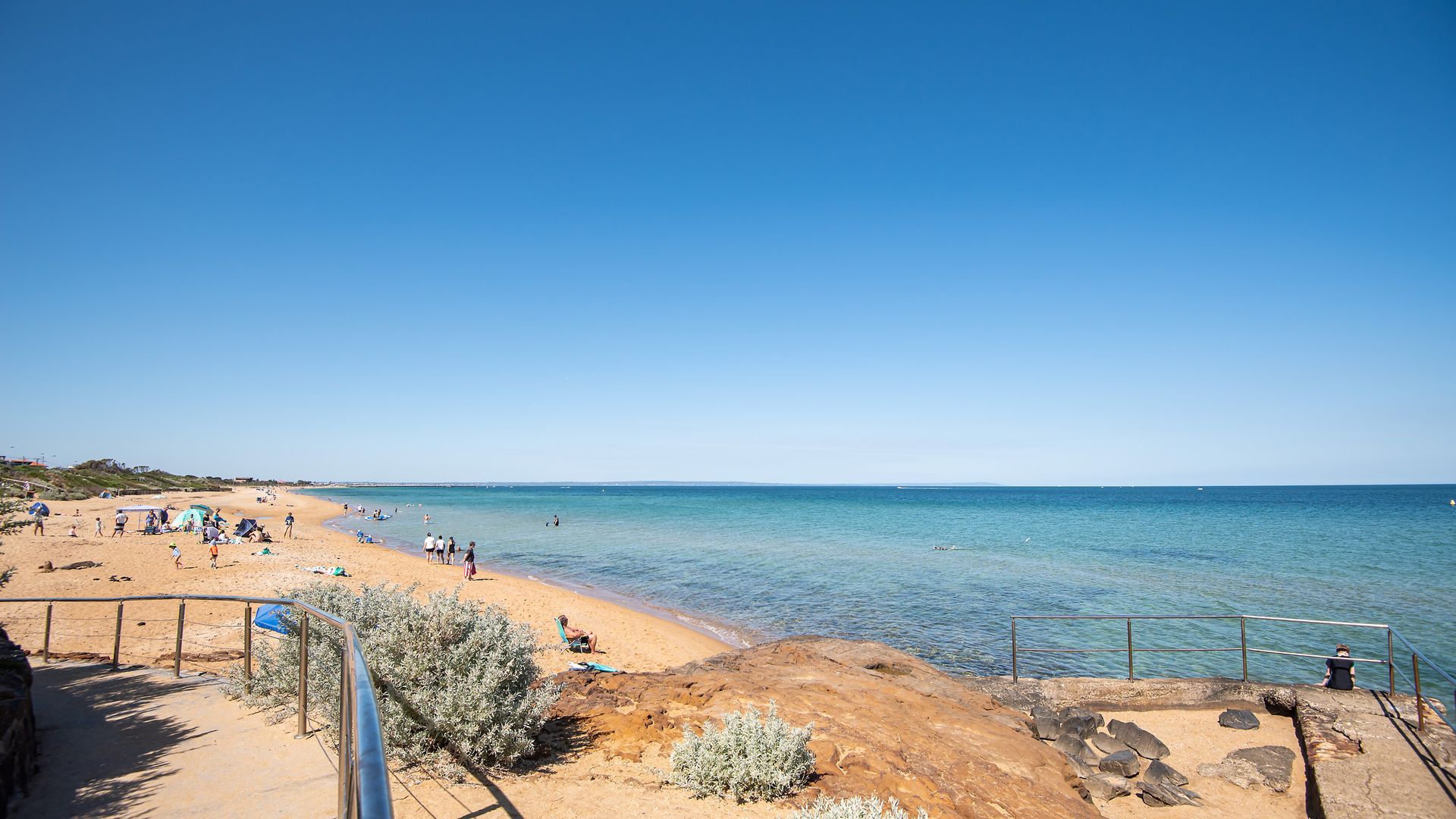 A beach with clear blue water, sandy shore, and rocky outcrops.