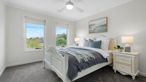 A bedroom with a bed, bedside tables, a ceiling fan, and a window with a view. - Parkdale Luxe | Pool, Walk to Beach & Shops (Parkdale)
