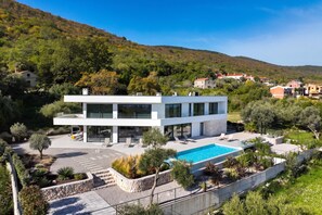 A modern two-story house with a swimming pool, surrounded by a landscaped garden and a hilly landscape. - Villa Alba (Rasa)