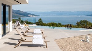 Ein moderner Poolbereich im Freien mit Liegestühlen und Blick auf das Meer und die Berge.