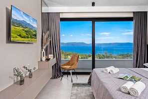Un dormitorio moderno con una cama grande, una silla, un televisor y vistas a un lago y montañas.