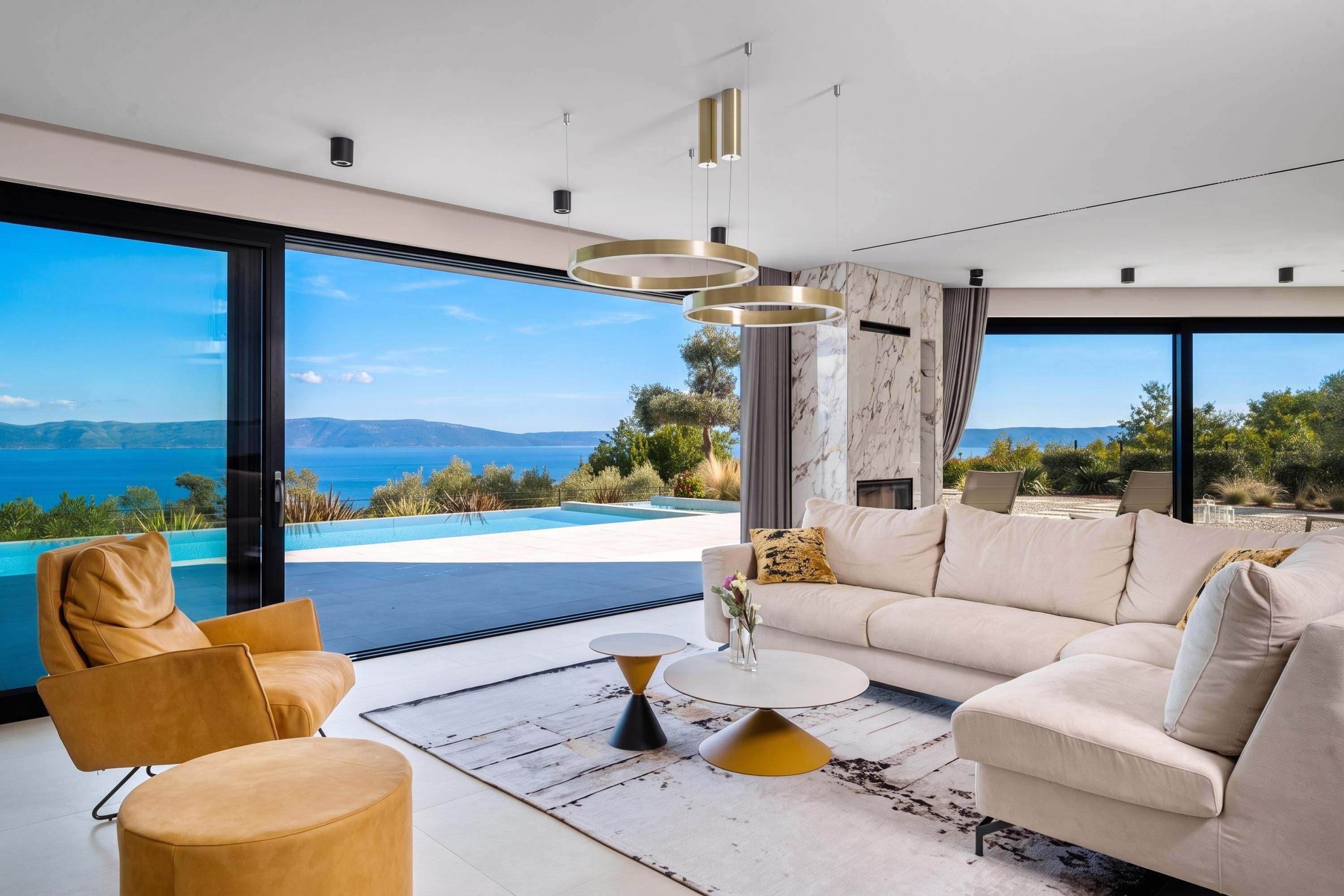 A modern living room with a sofa, coffee table, and chairs, overlooking a pool and mountains.