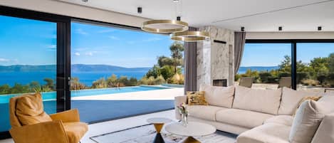 A modern living room with a sofa, coffee table, and chairs, overlooking a pool and mountains.