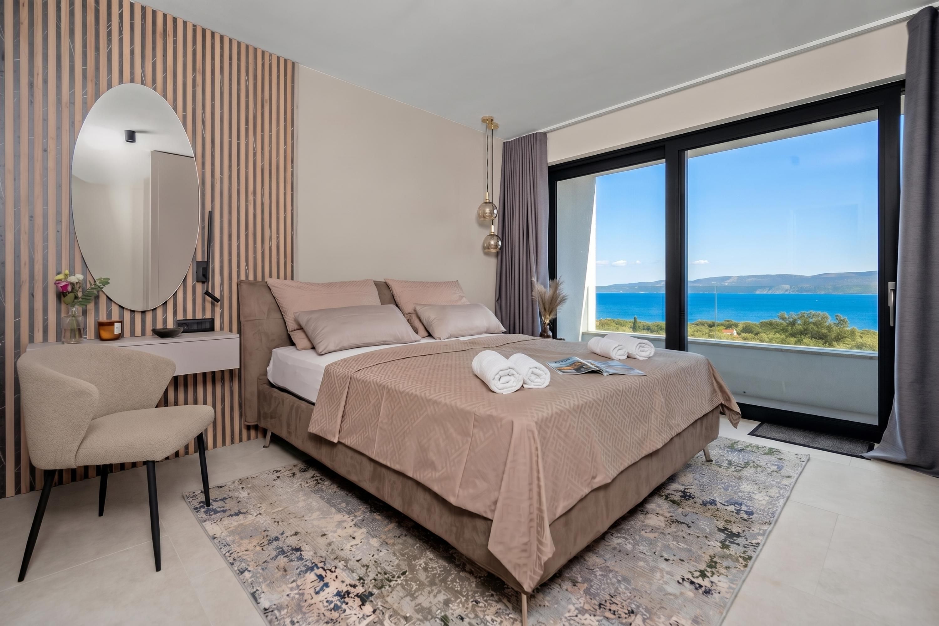 Un dormitorio moderno con una cama grande, un escritorio, una silla y vista al mar.