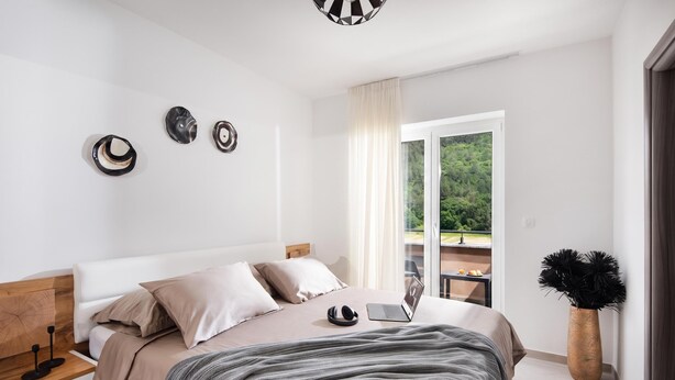 A modern bedroom with a bed, a laptop, and a view of a balcony with greenery. - Villa Terra With Pool & Sauna Near Rabac (Labin)