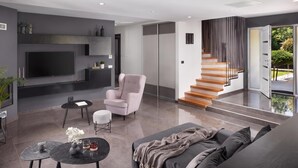 A modern living room with a flat-screen TV, a sofa, a chair, a coffee table, and a staircase leading to an outdoor area. - Villa Terra With Pool & Sauna Near Rabac (Labin)