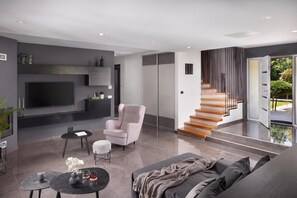 A modern living room with a flat-screen TV, a sofa, a chair, a coffee table, and a staircase leading to an outdoor area. - Villa Terra With Pool & Sauna Near Rabac (Labin)