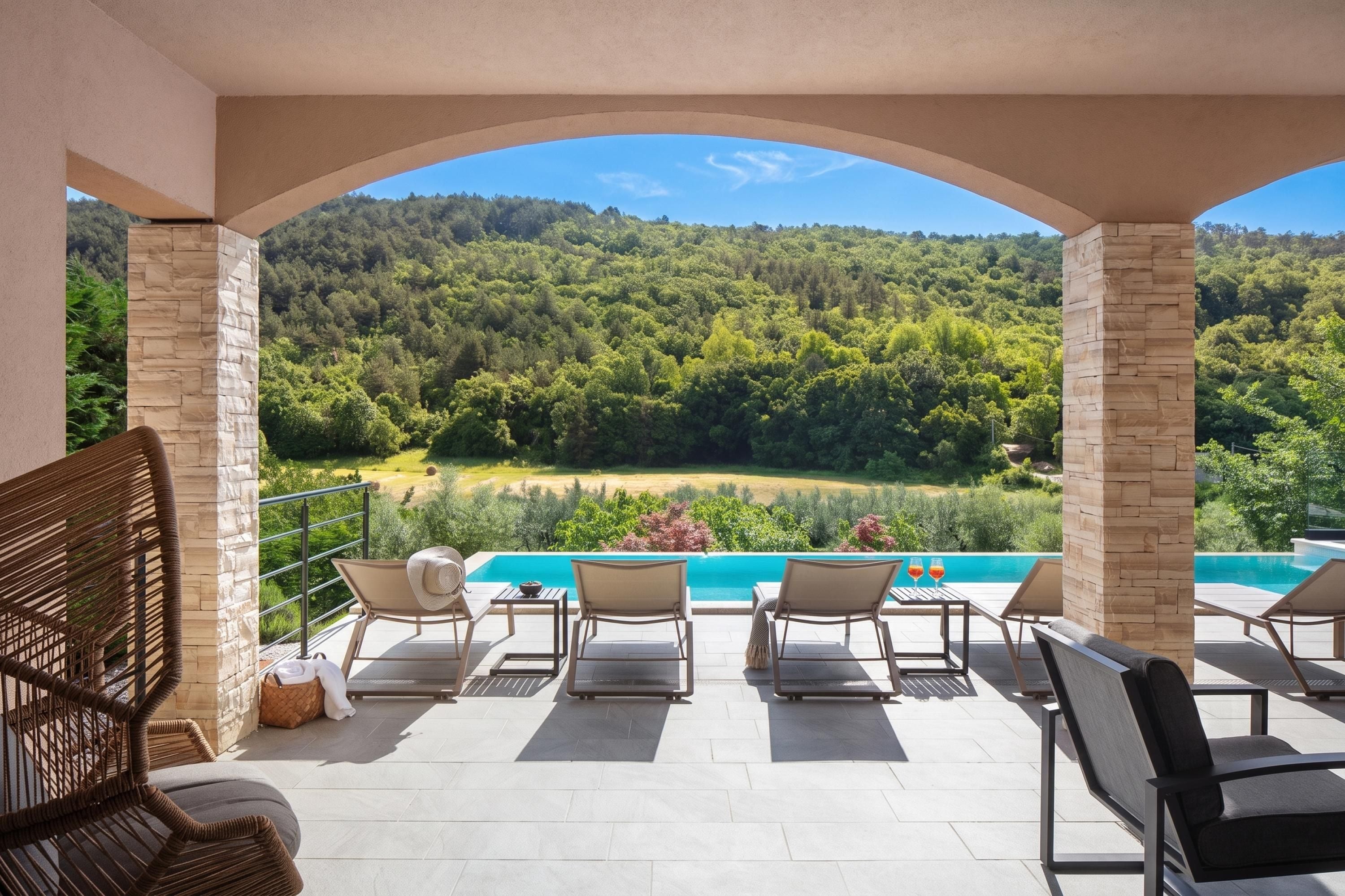 Una terrazza con poltrone relax e vista su un pendio boscoso e una piscina.