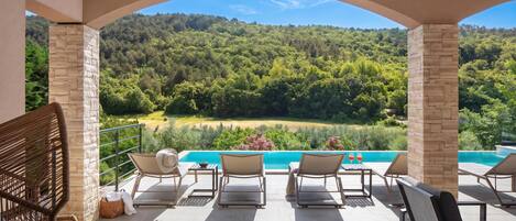 Una terrazza con poltrone relax e vista su un pendio boscoso e una piscina.