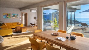 A modern living room with a wooden table, yellow chairs, and a sofa. There are paintings on the wall and a view of the sea through large windows. - Villa Saturea With Pool & Sauna Near Rabac (Labin)