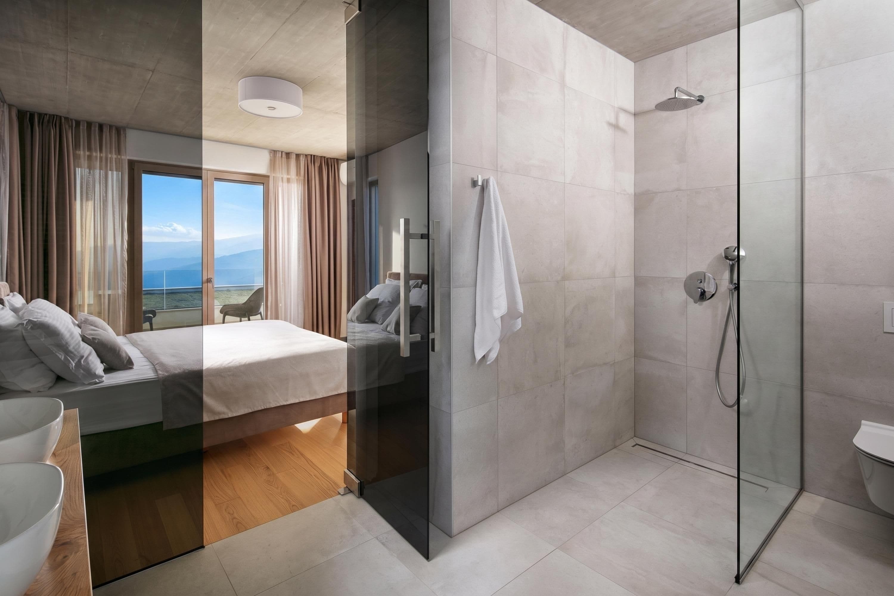 A modern hotel room with a bed, a shower, and a view of the sea.
