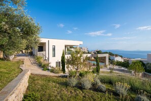 A modern house with a pool, surrounded by greenery and a clear view of the sea.