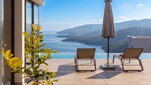 A terrace with two lounge chairs and an umbrella overlooking a body of water and distant mountains. - Villa Saturea With Pool & Sauna Near Rabac (Labin)