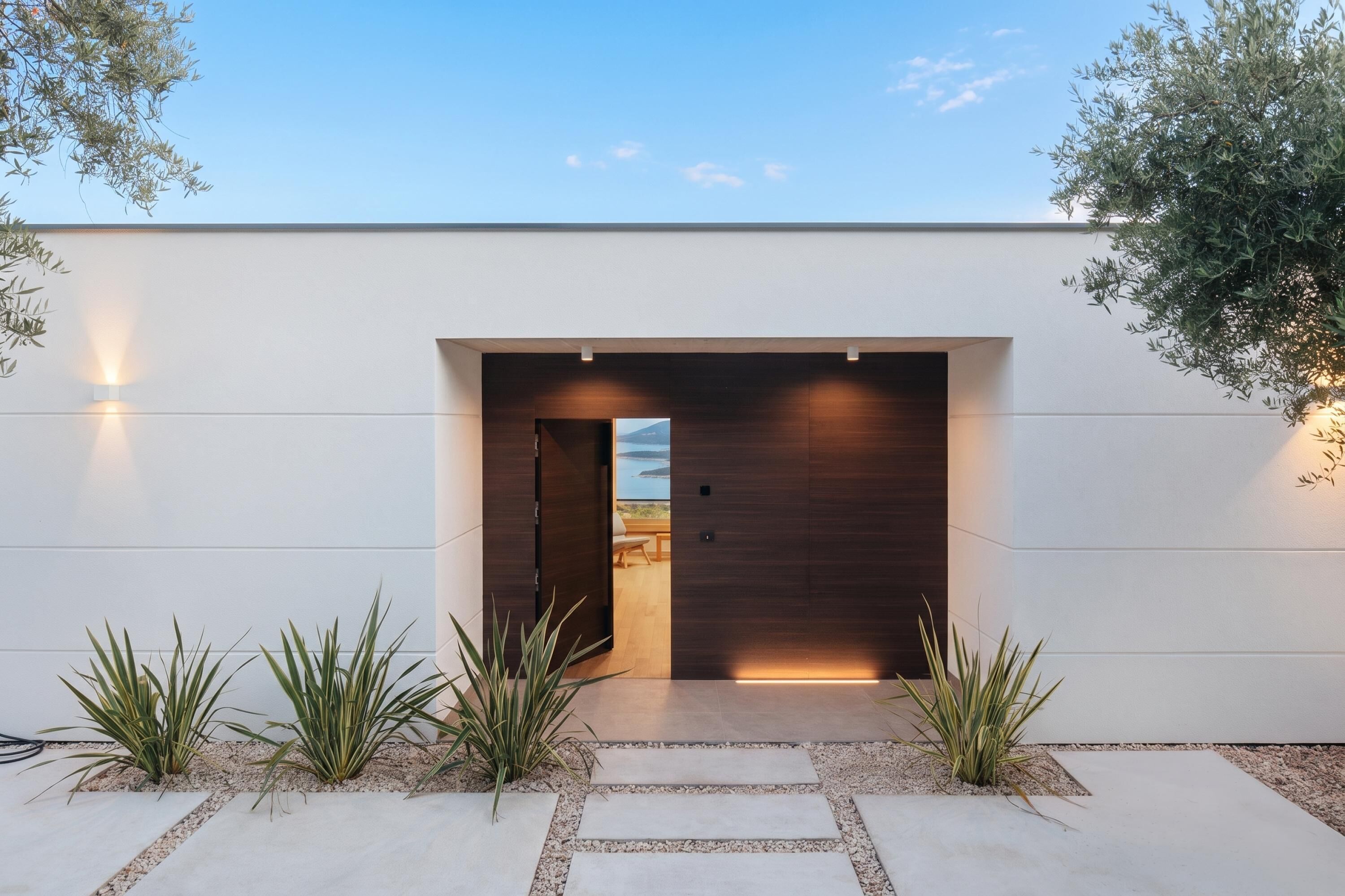 A modern building entrance with a glass door, a view of the outdoors, and a pathway leading to the door.