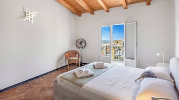 Ein Schlafzimmer mit einem Bett, einem Sessel, einem Ventilator und Blick auf die Stadt durch das Fenster.