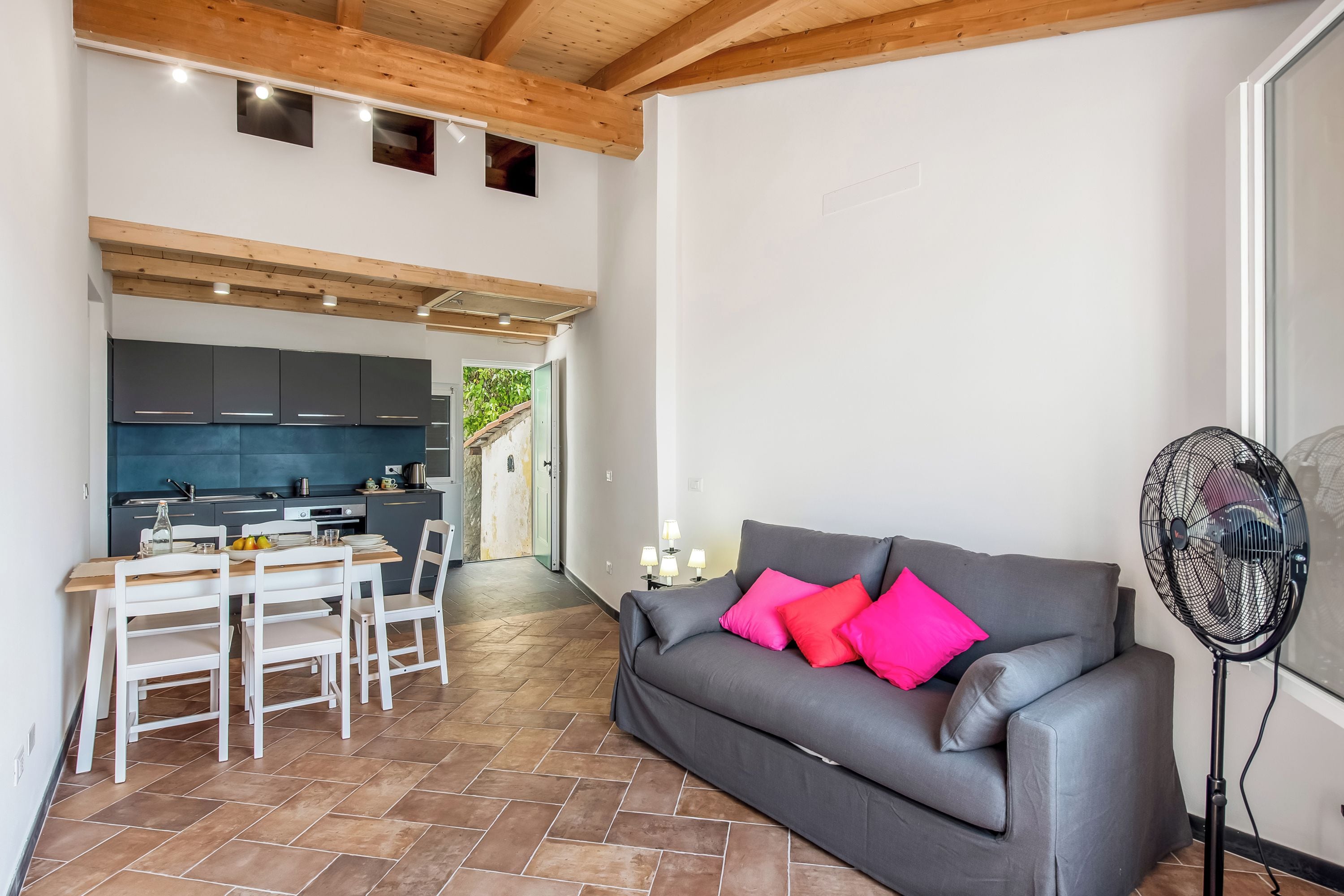 A modern living space with a grey sofa, white chairs, a dining table, and a kitchen area.