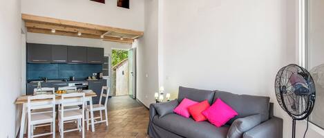 A modern living space with a grey sofa, white chairs, a dining table, and a kitchen area.