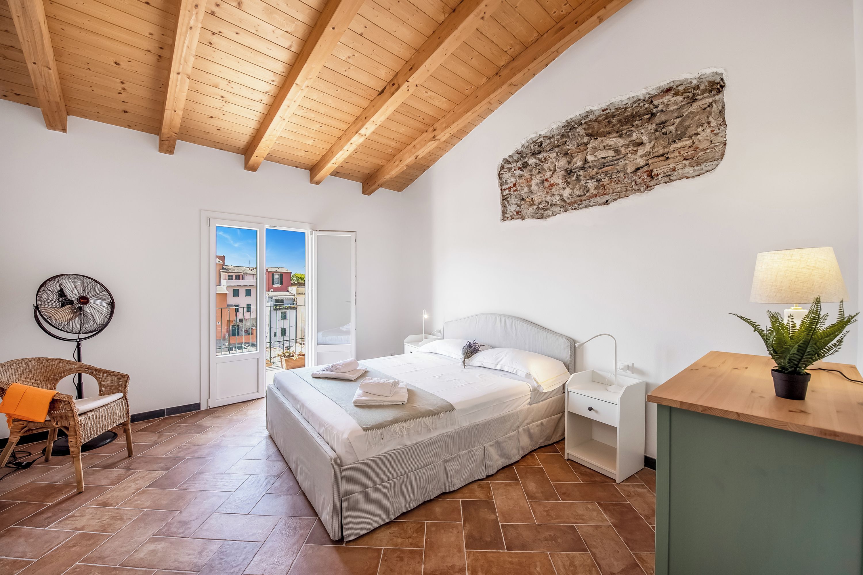 Une chambre à coucher avec un lit, une table de chevet, une lampe et une vue sur l’extérieur, visible à travers une porte.