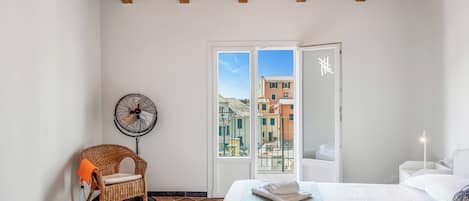 A bedroom with a bed, a chair, a fan, and a view of buildings through a door.