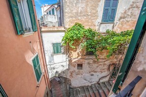 A narrow alleyway with buildings on either side, featuring a small window and a door with a metal gate. - High Roof Apartment (Vernazza)