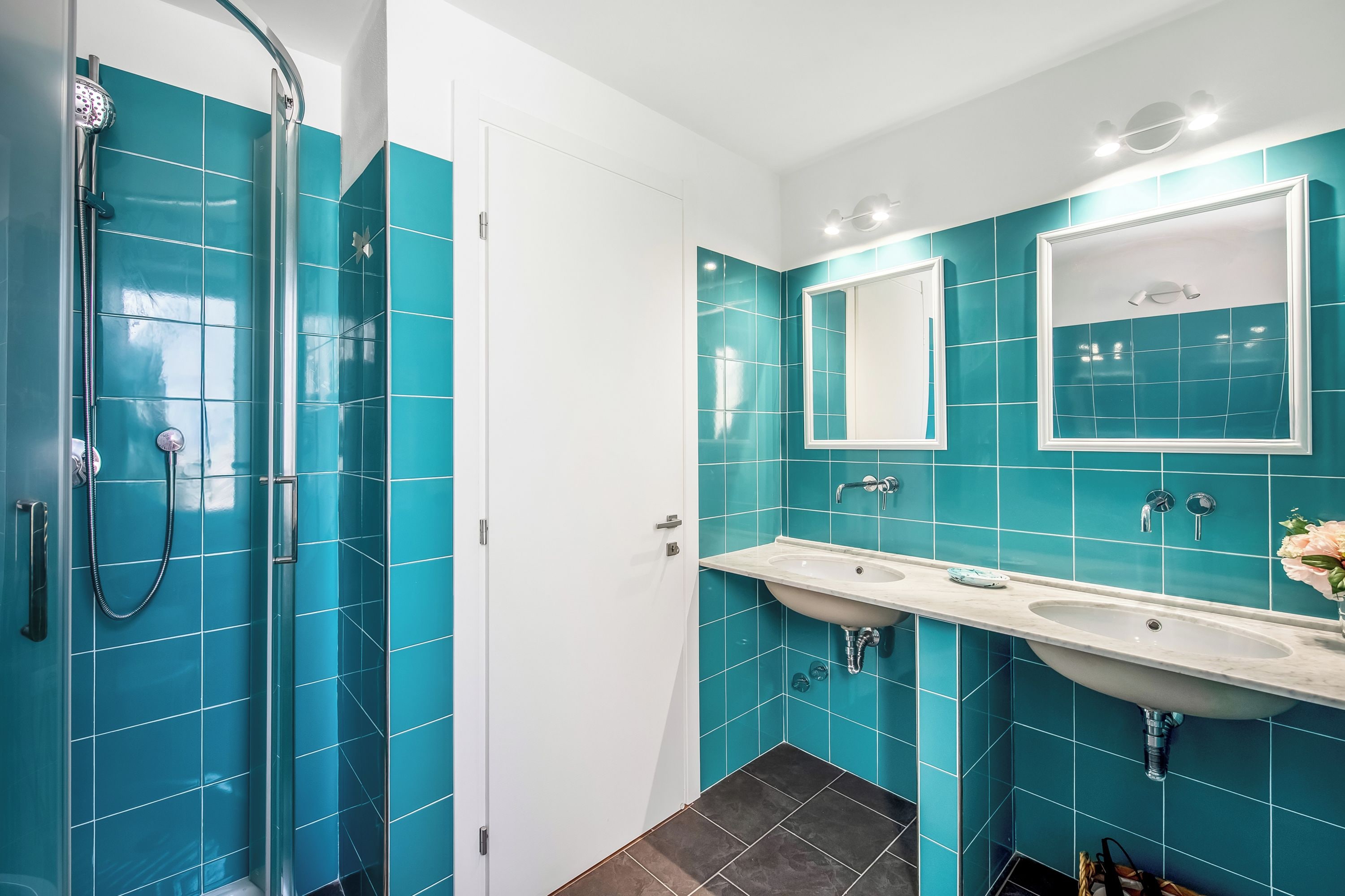 Un bagno con doccia, due lavandini e uno specchio.