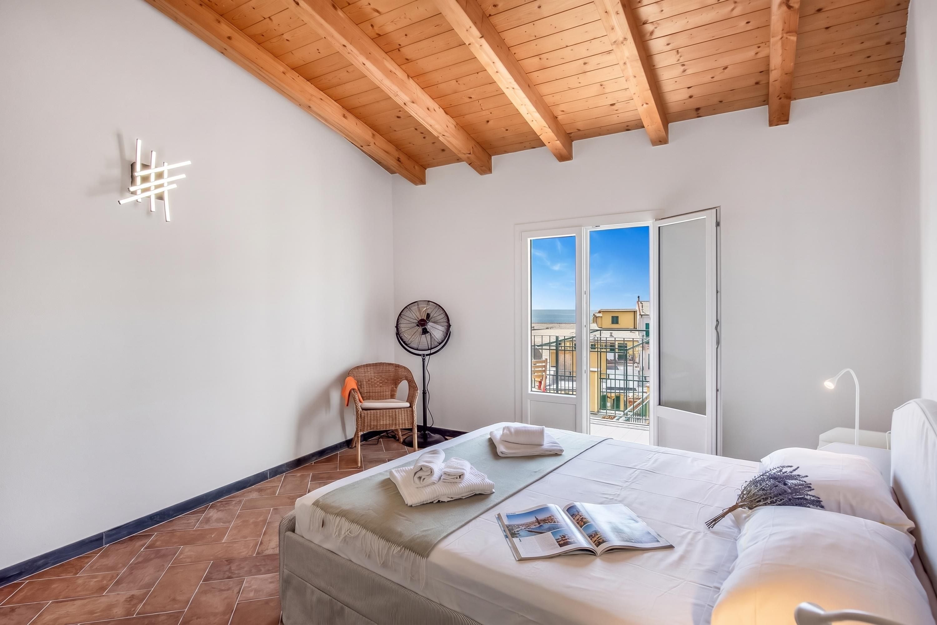 Una camera da letto con un letto, una ventola, una sedia e vista sulla città attraverso una finestra.