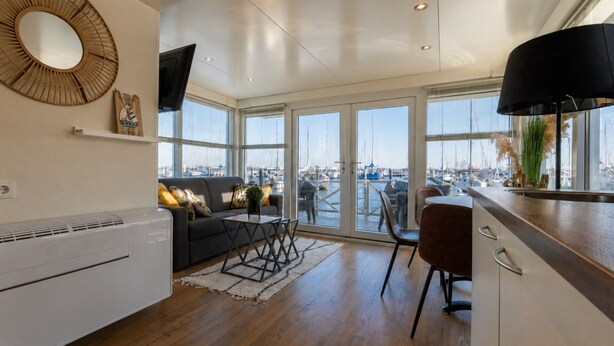 A modern living space with a sofa, dining table, and chairs, large windows with a marina view, and a kitchen area with a stove. - Enjoy in the harbor at Veerse Meer. (Wolphaartsdijk)