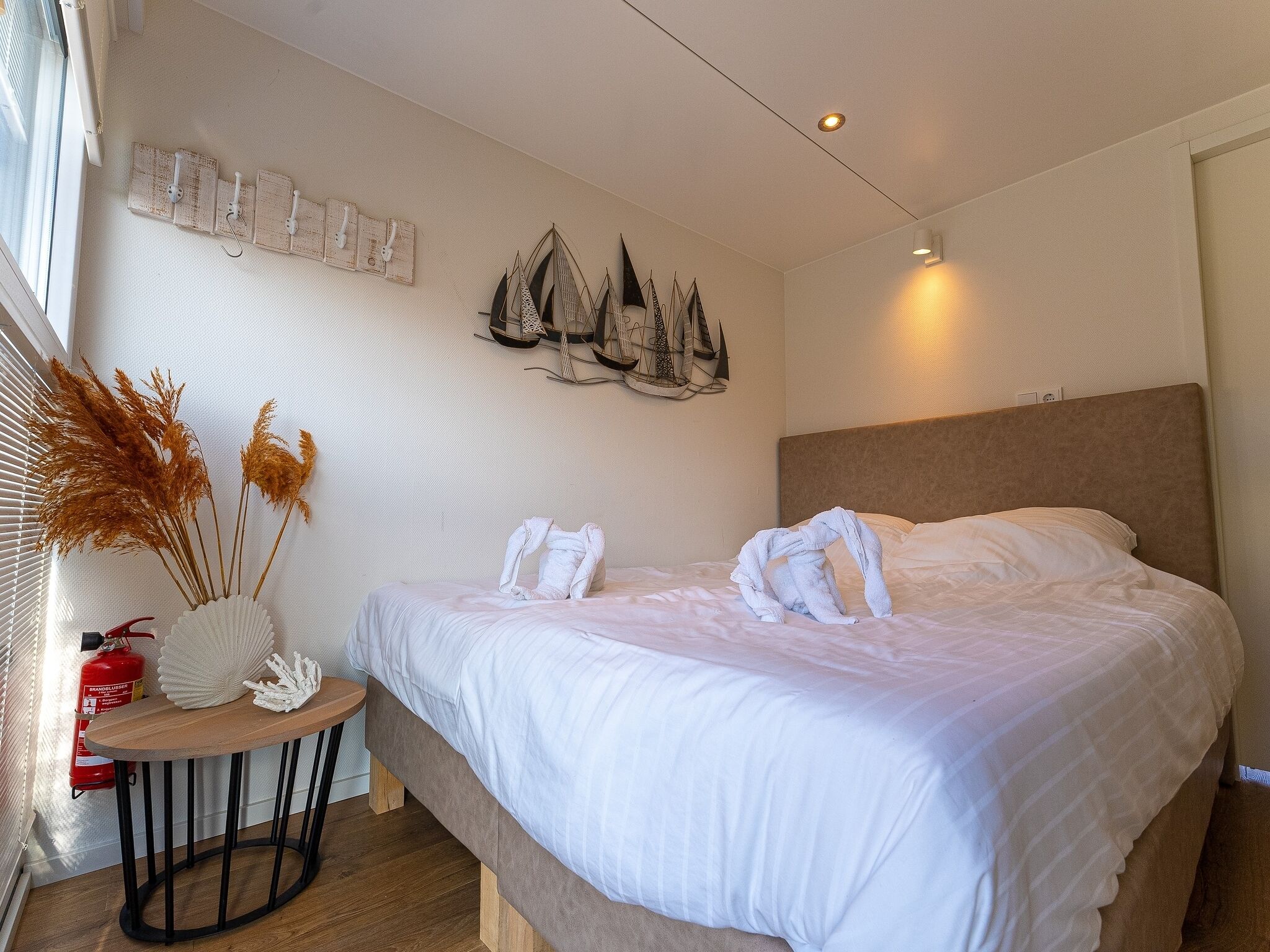 A hotel room with a large bed, a small round table with a vase of dried plants, and wall-mounted artwork.