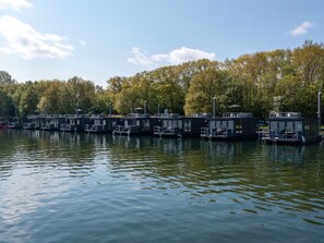 A series of floating structures with outdoor seating areas, connected by walkways, set against a backdrop of trees and a clear sky.