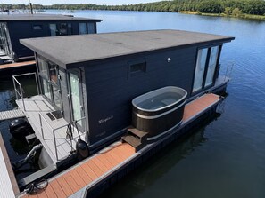 A floating houseboat with a hot tub, a covered deck, and a glass-enclosed area.