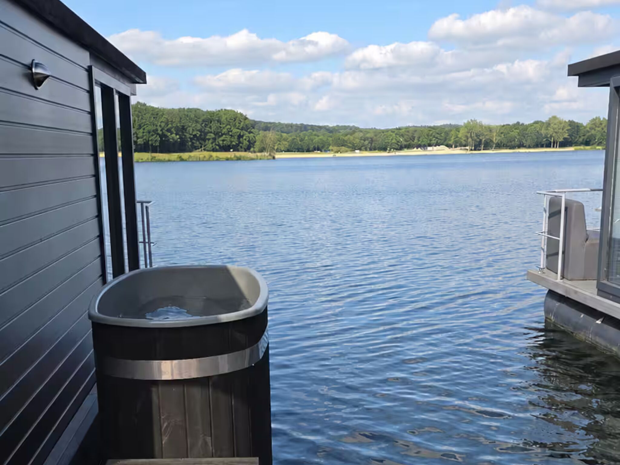 A boat docked by a calm lake with a wooden cabin and a hot tub.