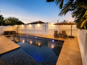 A swimming pool with a tiled deck, a seating area with chairs, and a wall with built-in lighting. - Baan Chang Retreat - Luxury Private Pool Villa (Bo Phut, Ko Samui)