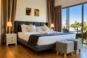 A hotel room with a large bed, two bedside lamps, a nightstand, a window with a view of palm trees, and a balcony. - Baan Chang Retreat - Luxury Private Pool Villa (Bo Phut, Ko Samui)