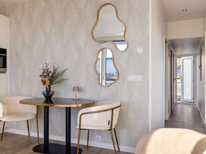 A modern dining area with a round table, two chairs, a vase with flowers, and two wall-mounted mirrors.