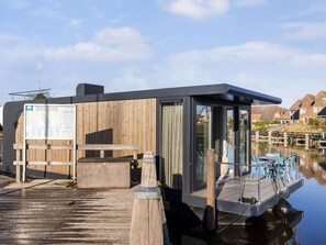 A floating structure with a wooden exterior, a glass door, and a small deck with chairs.