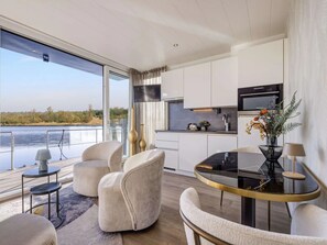 A modern kitchen with a view of a body of water, a dining area with a glass table, and a seating area with chairs.