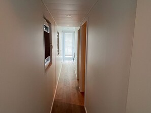 A narrow hallway with a wooden floor, white walls, and a door at the end.